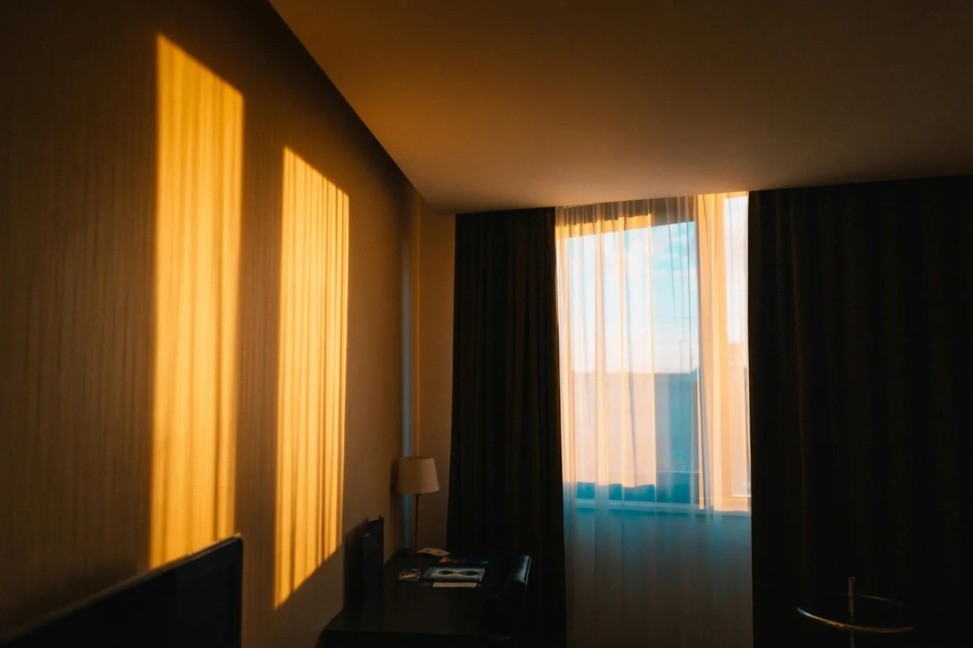 Una camera d’albergo con la luce dorata che entra dalle tende