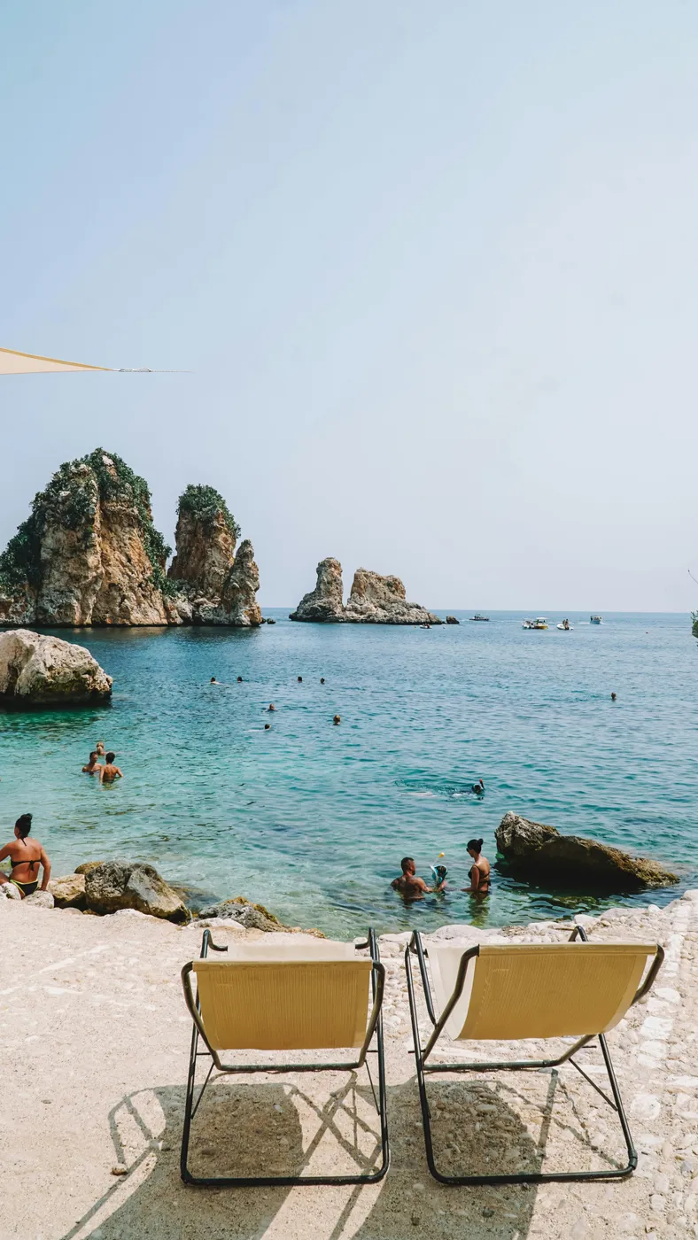 Due sdraio su una spiaggia siciliana con i faraglioni sullo sfondo